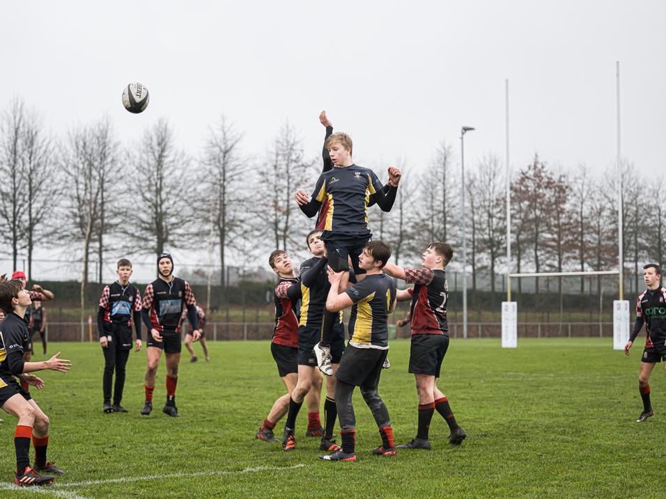 Jugendliche im Rugbyspiel heben einen Spieler in die Luft, während ein Rugbyball über den Platz fliegt.