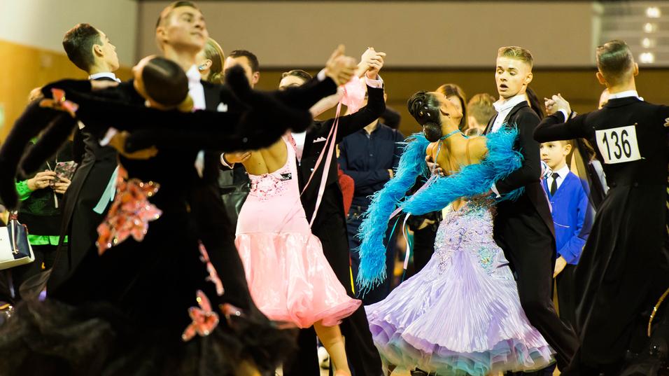 Tanzpaare in eleganten Kostümen tanzen auf einem Parkettboden bei einem Tanzwettbewerb.