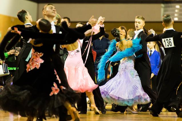 Tanzpaare in eleganten Kostümen tanzen auf einem Parkettboden bei einem Tanzwettbewerb.