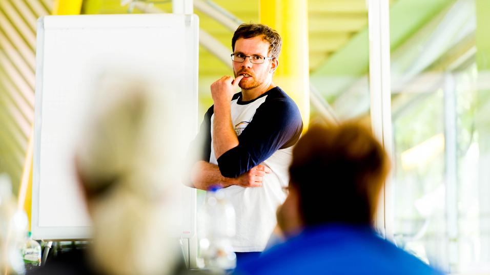 Mann mit Brille spricht vor einer Gruppe, ein Flipchart ist im Hintergrund sichtbar.