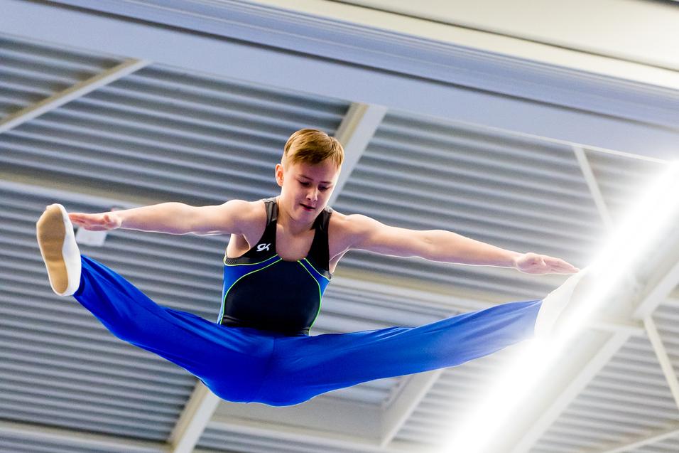 Ein Turner führt einen spektakulären Sprung mit gespreizten Beinen in einer Turnhalle aus.