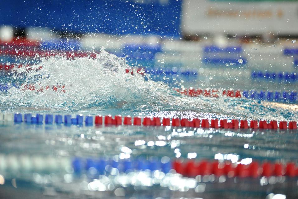 Spritzendes Wasser auf einer Swimmbahn mit roten und blauen Markierungen in einem Schwimmbad.