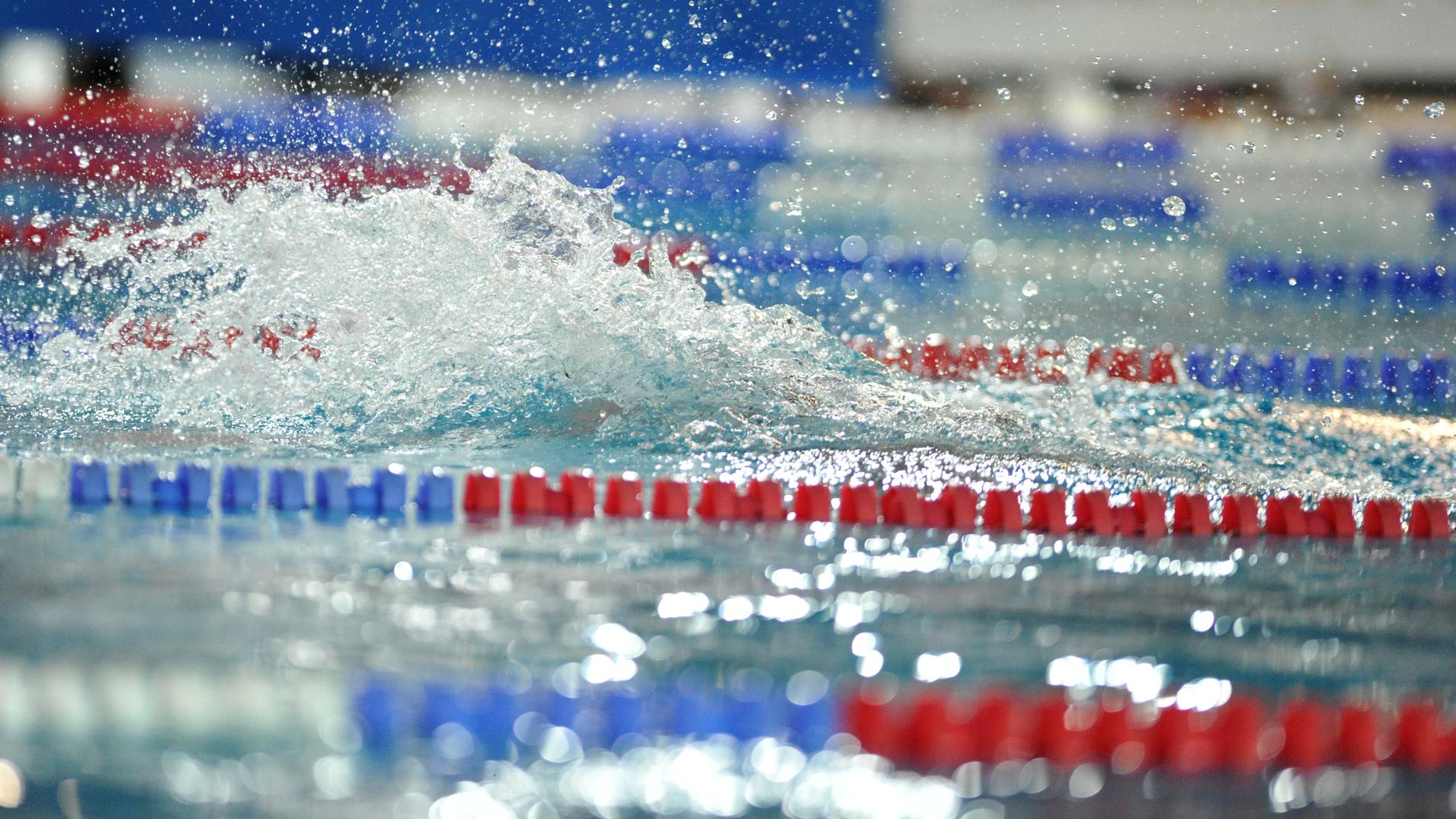 Spritzendes Wasser auf einer Swimmbahn mit roten und blauen Markierungen in einem Schwimmbad.