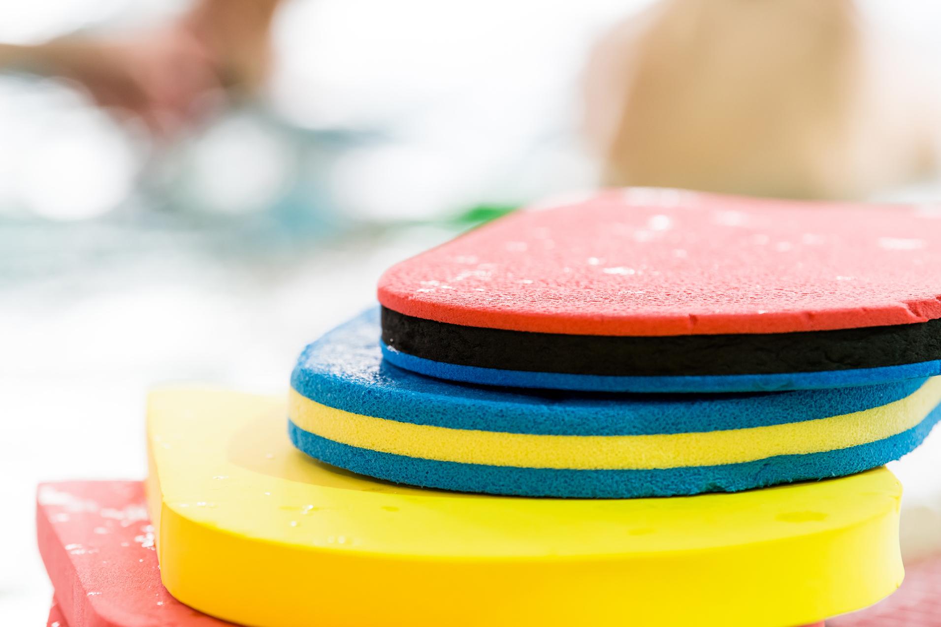 Bunte Schwimmbretter in verschiedenen Farben übereinander gestapelt, mit Wassertropfen auf der Oberfläche.