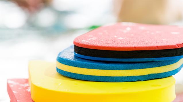 Bunte Schwimmbretter in verschiedenen Farben übereinander gestapelt, mit Wassertropfen auf der Oberfläche.